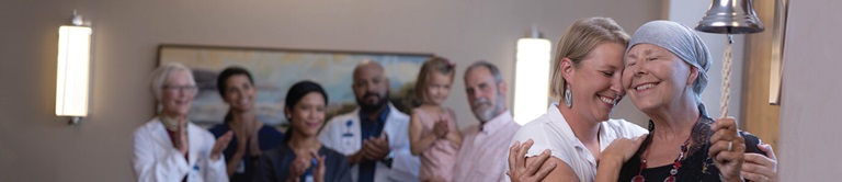 A Breast Cancer survivor ringing a bell while being encouraged by doctors and family