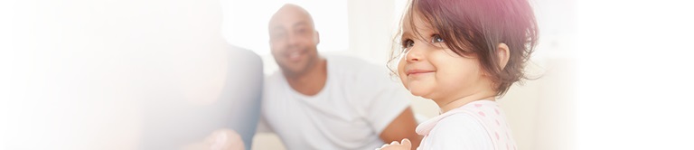 Little girl smiling with parents in the background
