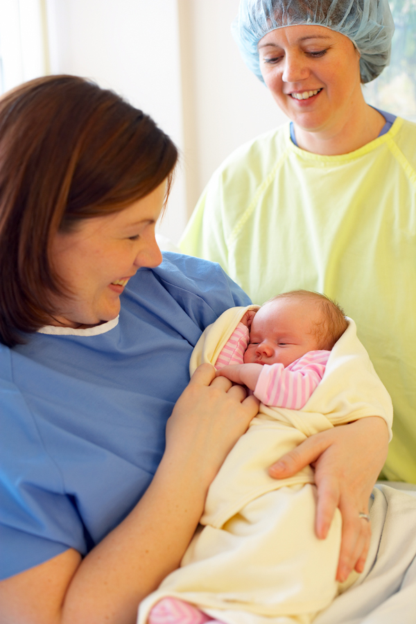 Midwife stands looking and mom and new baby