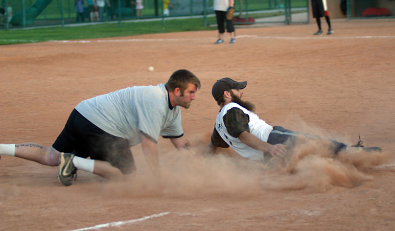 Recreational softball players hard slide into third base