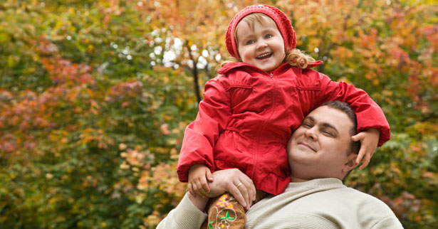 A overweight man lifts his daughter up on his shoulders outside in autumn